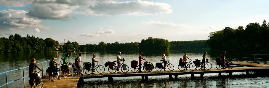 Blick aus der Ferne auf Radfahrende in Reihe auf einem Steg am Wasser. Copyright: Tanja Barthels