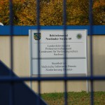 Blick durch den Zaun auf ein Schild in Dresden der sächsischen Sicherheitsbehörden.