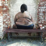 Mauergrafitti übergewichtige Frau in Unterwäsche von hinten. Vor der Mauer steht eine Bank, auf der links und rechts neben dem Motiv McDonaldsverpackungen liegen.