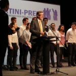 Mann hält Rede und steht vor den Schülerinnen und Schülern auf der Bühne