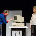 Foto von Schauspielerinnen beim Aufstand der Dinge. Eine Schauspielerin versucht einen alten Röhrencomputer mit Touch zu bedienen, während die andere hämisch schaut