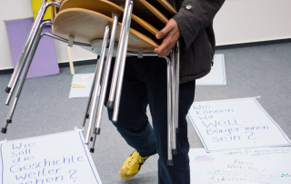 Eine Person schleppt gestapelte Stühle zwischen Collagen auf dem Boden