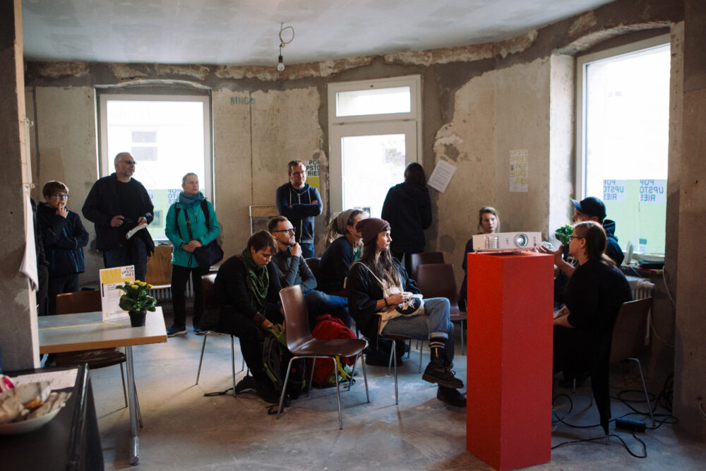 Eine Gruppe von Menschen sitzt bei den Pop-Up Stories vor einem Beamerbild Eine Gruppe von Menschen sitzt bei den Pop-Up Stories vor einem Beamerbild