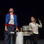 Zwei Schauspielerinnen schauen freudestrahlend in die Luft während sie ein altes Ergometer beziehungsweise ein altes Mikrofon verwenden.