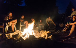 Sommerlager Teilnehmende sitzen entspannt im dunkeln im Sitzkreis am Lagerfeuer