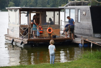 Ein kleiner Junge steht im Asa-FF Sommerlager 2018 am See und schaut auf ein überdachtes Boot, auf dem einige Menschen zu sehen sind