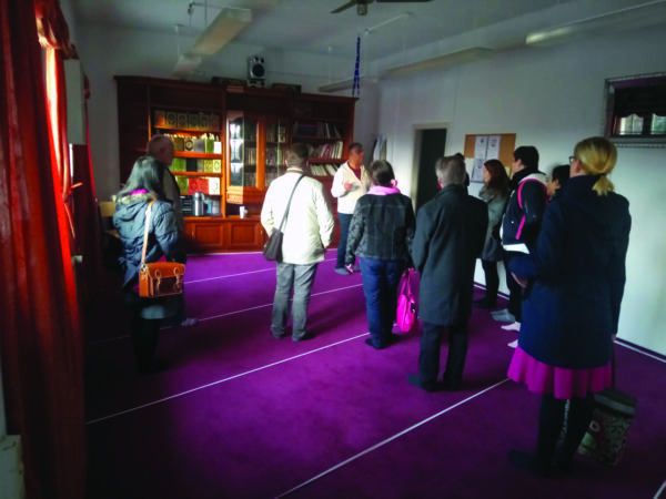 Einer Person erzählt eine Geschichte beim Rundgang in einem Raum mit einer Gruppe Einer Person erzählt eine Geschichte beim Rundgang in einem Raum mit einer Gruppe