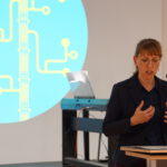 Eine Frau hält einen Vortrag, hinter ihr ist das Logo der Build Peace Konferenz an die Wand projiziert