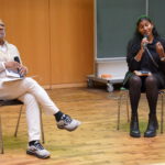 Zwei Menschen halten sitzend einen Vortrag in einem Hörsaal