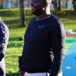 Ein Mann spricht im Freien auf einem Fußballfeld, er trägt Fußballkleidung