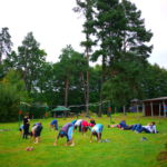 Gruppe beim Sport im Freien während eine Gruppe dahinter faulenzend auf der Wiese liegt.