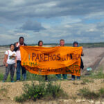 Am Grubenrand Aktivistinnen und Aktivisten vor einem Braunkohletagebau halten ein Transparent "Paremos La Mina - Klimagerechtigkeit"