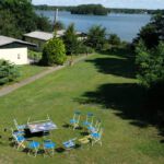 Foto von oben auf den See und einen leeren vorbereiteten Stuhlkreis mit einem Tisch und vorbereiteten bunten Zetteln auf der Wiese vor dem See