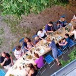 Blick von oben auf einen langen Tisch, an dem alle Teilnehmenden des Sommerlagers gemeinsam im Freien essen zur Ankündigung des Sommerlagers