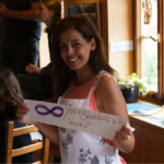 Lächelnde Teilnehmerin hält Papier in der Hand worauf steht: "8 young Leaders with impact"