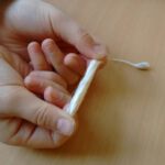 Nahaufnahme von einem Tampon, der zwischen zwei Daumen und Zeigefingern gestreckt wird