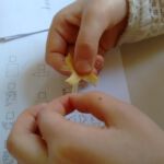 Ein Stück Stoff wird von zwei Händen über einer Anleitung bearbeitet