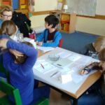 Schülerinnen und Schüler am Gruppentisch mit einer Referentin