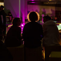 Foto © Mark Frost Drei Personen von hinten sitzen zusammen bei der Eröffnung des Aufstands der Geschichten