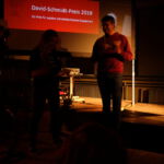 Bühne bei Preisverleihung des David-Schmidt-Preises 2019 mit zwei lachenden Personen im Dunkeln