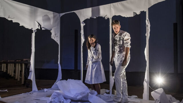 Foto: Nasser Hashemi Eine Shauspielerin und ein Schauspieler blicken entsetzt auf die Überreste einer zerschnittenen Wand, die aus Papier war und mit Text bekritzelt war