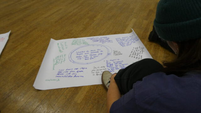 Ein Plakat im Rahmen von Wir.Wie mit viel Text, worüber sich eine Teilnehmerin lehnt