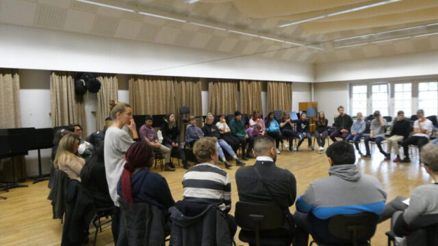 Schülerinnen und Schüler der Wir.Wie Besetzung sitzen in einem großen Stuhlkreis