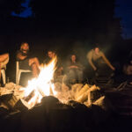 Sommerlager Teilnehmende sitzen entspannt im dunkeln im Sitzkreis am Lagerfeuer